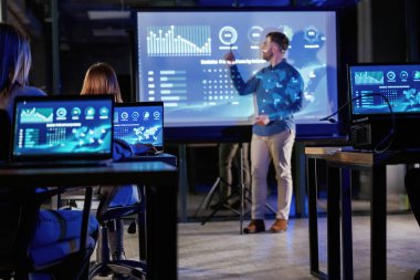 Resmi kıyafetlerle. Erkek işletme eğitmeni projektöre karşı, insanlara öğretiyor..