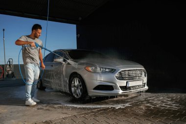 Gümüş renkli yüzey, otomobili yıkıyor. Adam dışarıda arabasıyla bekliyor..