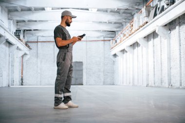 Elinde siyah dijital tablet var. Erkek işçi boş depoda..