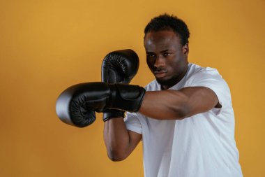 Boks yumruğu alıştırması yapıyorum. Siyah adam sarı arka plana karşı..