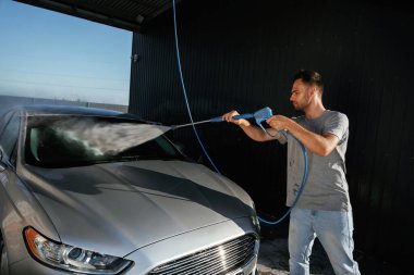 Gümüş renkli yüzey, otomobili yıkıyor. Adam dışarıda arabasıyla bekliyor..