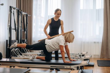 Sırt egzersizi. Kadın eğitmen yaşlı kadının egzersiz yapmasına yardım ediyor..