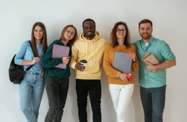 Not defterleri ve kahve fincanı tutuyor. Bir grup genç beyaz arka planda duruyor..