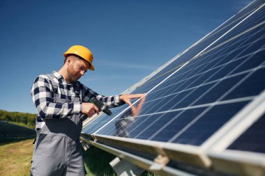 Neredeyse bitti, matkap kullanarak kurulum yapılıyor. Gündüz vakti fotovoltaik güneş panelleri olan bir mühendis..