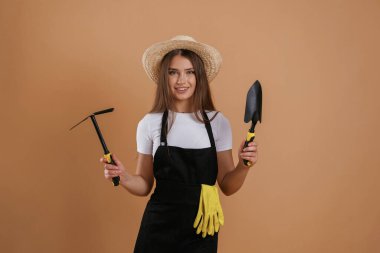 Bahçıvan aletleriyle çiftçi. Genç ve güzel bir bayan stüdyoda arka plana karşı..