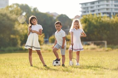 Futbol topu ve badminton raketleri. Mutlu çocuklar yaz tarlasında.