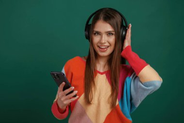 Kulaklıkla müziğin tadını çıkarma anı. Genç bir kadın stüdyoda yeşil arka plana karşı duruyor..