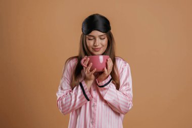 Pembe pijama, bir bardak da içecek. Genç ve güzel bir bayan stüdyoda arka plana karşı..