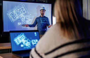 Erkek mimar, insanlar için mavi projektör üzerinde inşaat alanı projesi gösteriyor.