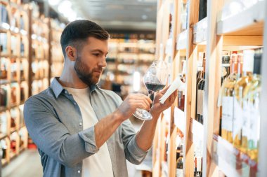 İçkiyle bardağa bakıyorum. Adam dükkanda şarap seçiyor..