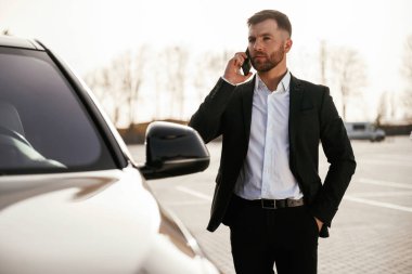 Telefonla konuşarak. Takım elbiseli bir işadamı dışarıda siyah arabasının yanında..