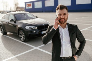 Telefonla konuşarak. Takım elbiseli bir işadamı dışarıda siyah arabasının yanında..