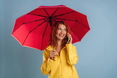 Kırmızı şemsiyeli, telefon başında sohbet. Kadın stüdyoda arka planda..