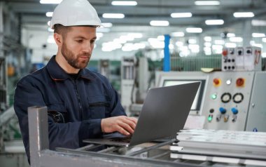 Dizüstü bilgisayarı kullanarak. Fabrika işçisi kasketli bir şekilde içeride..