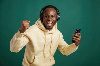 Kulaklıkla, müzikten zevk alarak. Afrikalı Amerikalı adam stüdyoda yeşil arka plana karşı duruyor..