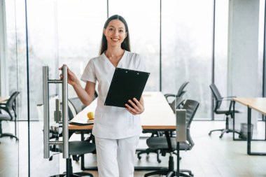 Ön manzara. Elinde not defteriyle dikiliyorsun. Beyaz önlüklü kadın doktor içeride..