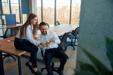 Telefonda bilgi gösteriliyor. Kadın ve erkek çalışanlar ofiste çalışıyor..