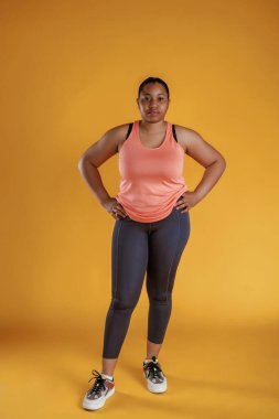 Spor kıyafetleri içinde. Afrikalı Amerikalı kadın sarı arka planda stüdyoda..