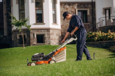 Yandan manzara, çim biçme makinesiyle çim biçme. Bahçede profesyonel bahçıvan var..