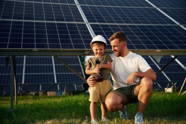Elinde matkapla poz veriyor. Baba ve küçük oğlu güneş panellerinin yakınındalar..