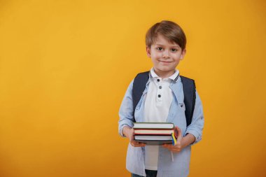 Okul için hazır, elinde kitaplarla. Küçük çocuk sarı arka planda stüdyoda..