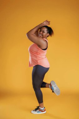 Yan görünüş, poz verme. Tozluklarla. Afrikalı Amerikalı kadın sarı arka planda stüdyoda..