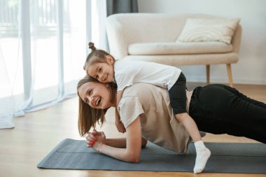 Annemin sırtüstü yatıyorum. Küçük kızı olan genç bir kadın evde yoga yapıyor..