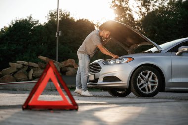 Güneş ışığı altında, kırmızı tabela, kaza, bozuk otomobil, tamir. Adam dışarıda arabasıyla bekliyor..