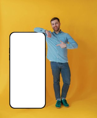 Kopya alanı için büyük akıllı telefonlu. Mavi gömlekli çekici adam sarı arka plana karşıdır..
