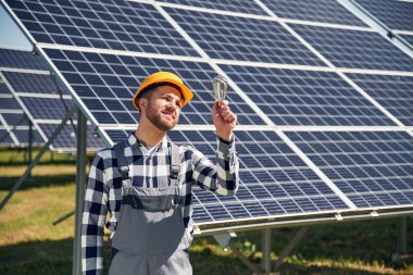 Geleneksel ampul elinde. Gündüz vakti fotovoltaik güneş panelleri olan bir mühendis..