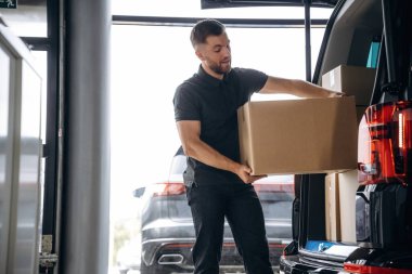 Teslimatçı ya da yükleyici elinde bir kutuyla arabanın yanında..