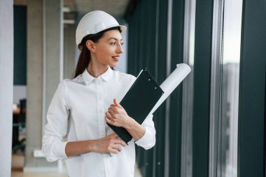 Plan ve not defteri elimde. Kasketli ve beyaz elbiseli kadın mimar içeride..