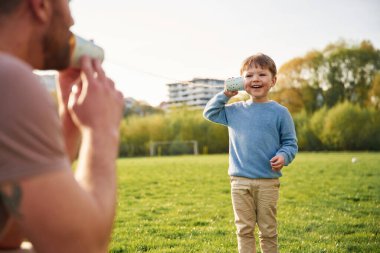 Kağıt bardak telefon kullanarak. Mutlu baba ve oğul yazın sahada eğleniyorlar..