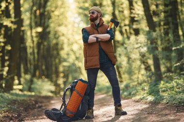 Sarı balta elinde, sırt çantası yerde. Sakallı adam gündüz vakti ormandadır..