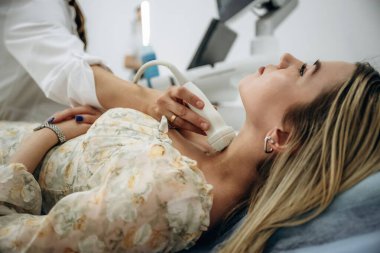 Yan görüş. Kadın uzanıyor ve tiroid bezinin ultrasonik testinden geçiyor..