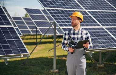 Ellerinde not defteriyle sahada. Gündüz vakti fotovoltaik güneş panelleri olan bir mühendis..