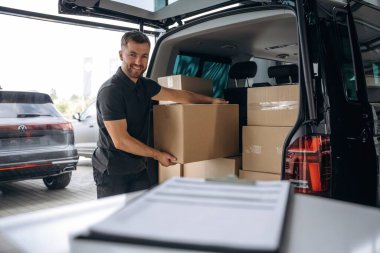 Teslimatçı ya da yükleyici elinde bir kutuyla arabanın yanında..