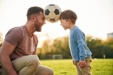 Futbol topu, kafasından tutmak, eğlence. Mutlu baba ve oğlu yazın sahada olurlar..
