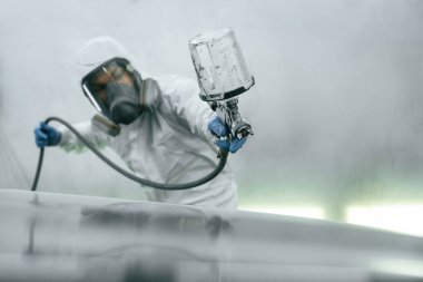 Koruyucu maskeyle ve giyerek. Spreyciyle araba boyayan adamın yakın görüntüsü..