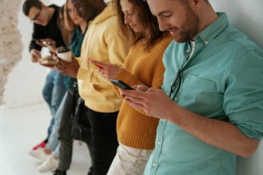 Yan görüş. Elinde akıllı telefonlarla. Bir grup genç beyaz arka planda duruyor..
