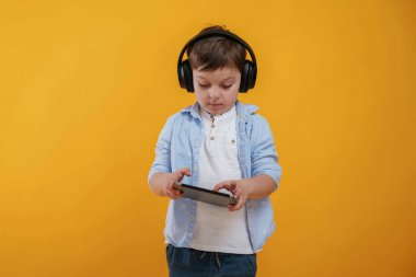 Tablet ellerde. Küçük çocuk sarı arka planda stüdyoda..