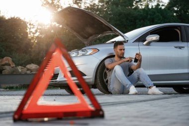 Kırık araba, kırmızı işaret. Adam dışarıda arabasıyla bekliyor..