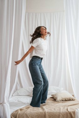 Eğleniyor, zıplıyor. Genç ve güzel bir kadın evde, yatağın üzerinde..