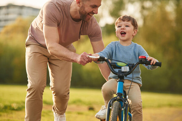 Синий велосипед, езда верхом. Счастливый отец с сыном веселятся на поле летом.