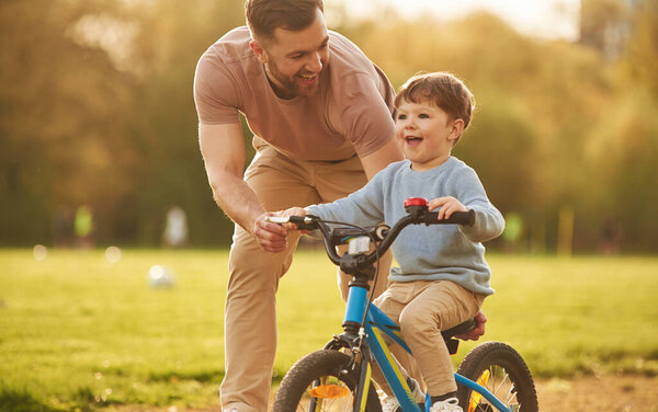 Синий велосипед, езда верхом. Счастливый отец с сыном веселятся на поле летом.