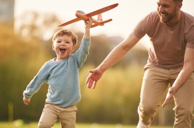 Yüksekten uçmak, oyuncak uçak tutmak, koşmak. Mutlu baba ve oğul yazın sahada eğleniyorlar..