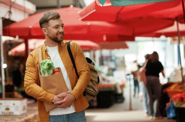 Neşeli, kağıt torbada ürünleri var. Yakışıklı adam sokak pazarında ya da pazarda..