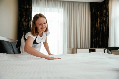 Yatakla ilgilenmekle meşgulsün. Genç oda hizmetçisi otel odasında..