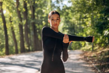 Egzersizleri ısıt. Genç, sıska kadın dışarıda siyah spor kıyafetleri giyiyor..