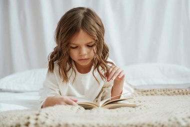 Kitapla birlikte yatağa uzanmak. Şirin küçük kız evde..